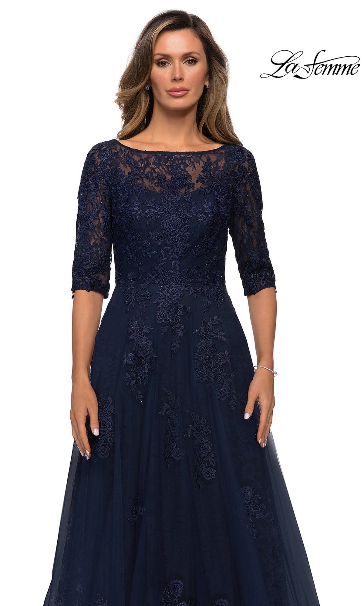 Woman in a navy blue Long Formal Dress: La Femme 28036 with lace bodice, half sleeves, and tulle A-line skirt, posing against a plain white background. La Femme logo at top right.